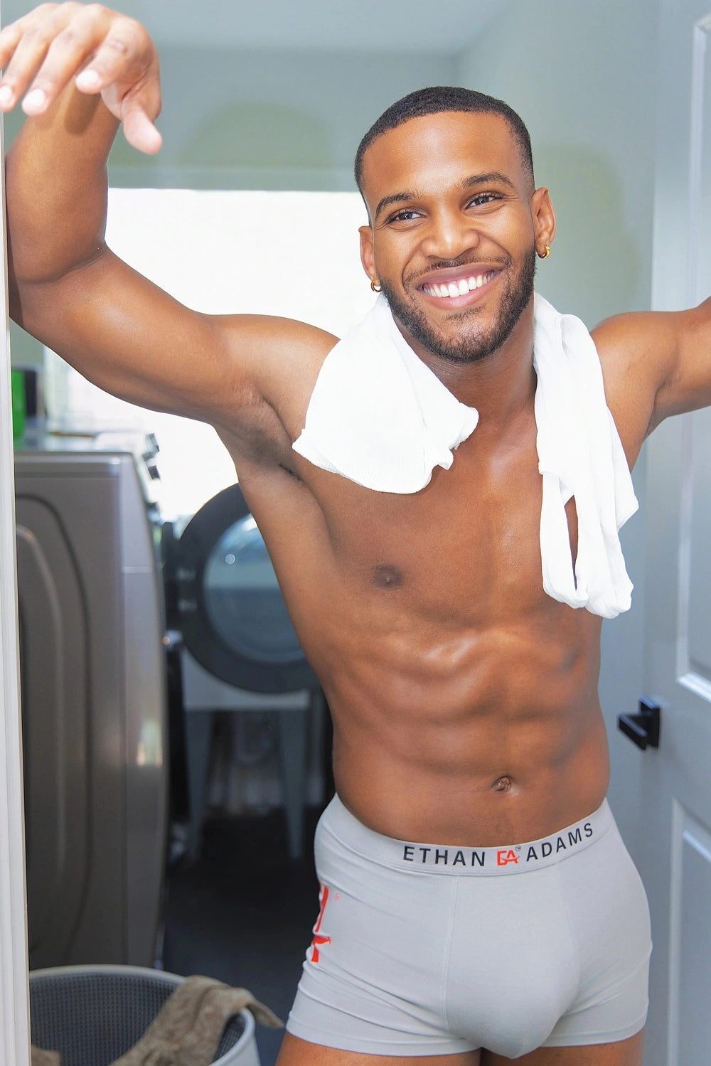 Man in gray underwear with 'Ethan Adams' brand logo, standing in a laundry room. shop the comfort Ethan Adams